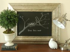 a framed chalkboard with birds on it next to a potted plant and books