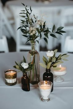 two vases filled with flowers and candles on top of a white table cloth covered table