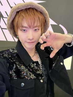 a young man with red hair wearing a black jacket and silver earrings pointing at the camera