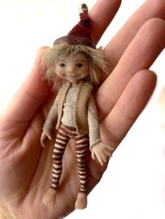 a hand holding a small doll with a hat on it's head and striped pants