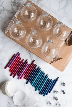 an assortment of colored candles and other items on a marble counter top with a cardboard box