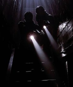 two people sitting on stairs in the dark with their arms around each other and lights shining down