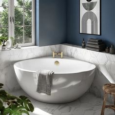 a white bath tub sitting in a bathroom next to a window and a wooden stool