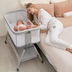 a woman laying in bed next to a baby in a bassinet and changing table