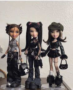 three dolls are standing on top of a table with one holding a purse and the other wearing boots