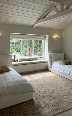 two beds in a room with white walls and carpeted flooring next to windows