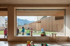 children looking out the window at an outside area with toys on the floor and in front of them