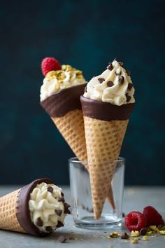 three ice cream cones with chocolate and raspberries in them on a gray surface