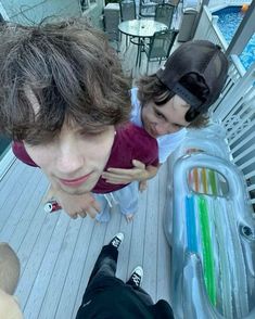 two young men standing next to each other on top of a wooden floor near a pool