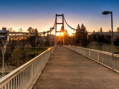 the sun is setting over a bridge that has a metal railing on one side and a light pole on the other