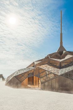 an unusual building sits on the beach with sand blowing in front of it and blue skies above