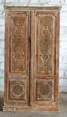 an old wooden armoire with carvings on the front and side panels, sitting against a white brick wall