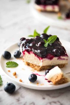 a piece of cheesecake with blueberries and mint on a plate next to it