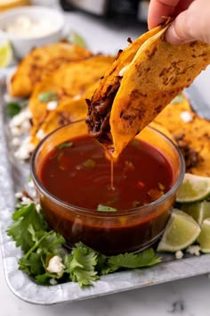 a person dipping tortilla chips into a bowl of chili and cilantro sauce