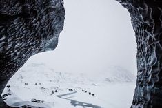 a group of people walking up the side of a snow covered mountain under an ice cave