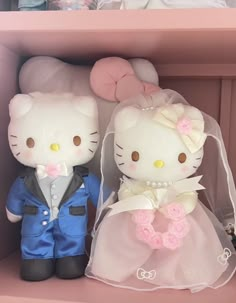 two hello kitty dolls are dressed up in wedding attire and tuxedo, sitting on a pink shelf