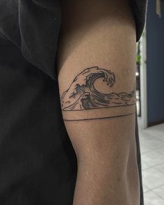 a man with a tattoo on his arm is standing in front of the ocean waves