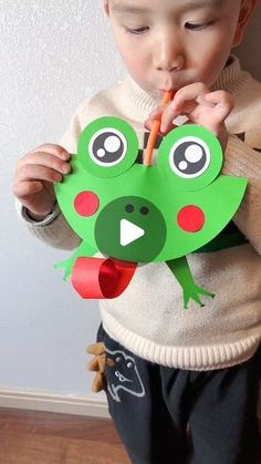 a young boy is holding a paper cut out of a frog with a carrot in his mouth