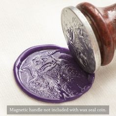 a purple wax seal sitting on top of a white cloth next to a wooden stamp