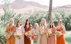 a group of women standing next to each other in front of a palm tree and mountains