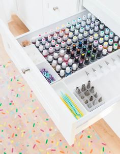 an open drawer filled with crafting supplies on top of a floor covered in sprinkles