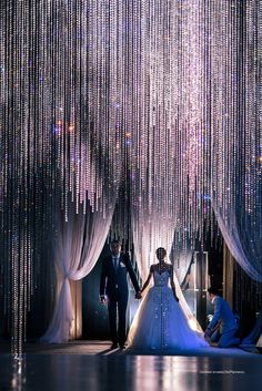 the bride and groom are walking down the aisle with beaded curtains hanging from the ceiling