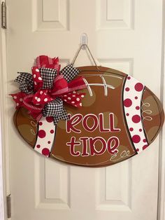 a football shaped door hanger with the word roll tide painted on it and a polka dot bow