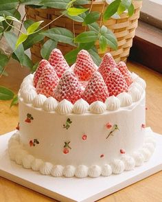 a white cake topped with strawberries on top of a table next to a potted plant