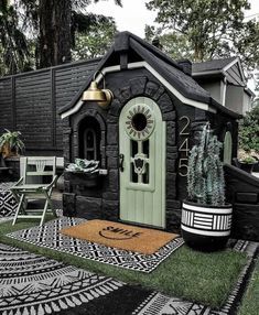 a small black and white house with a green door on the front lawn, surrounded by potted plants