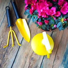 three yellow garden tools sitting on top of a wooden table next to flowers and a potted plant