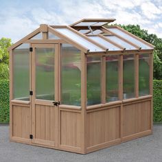 a small wooden greenhouse with glass doors on the roof and side walls, in front of a hedge