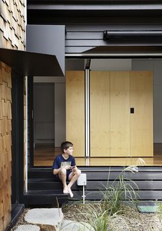 a young boy sitting on the steps in front of a house with wood sidings