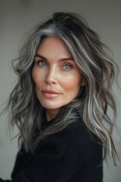 Woman with striking grey hair and blue eyes, gazing directly at the camera with a subtle smile, against a neutral background. Gray Hair Blending, Grey Brown Hair, Grey Hair Transformation, Black Cake, Gray Hair Growing Out