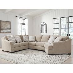 a large sectional couch with pillows on it in front of two windows and a rug