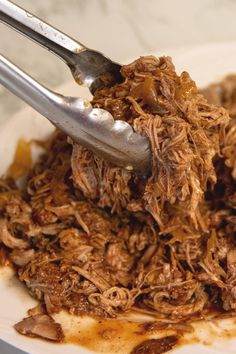 a white plate topped with shredded meat and a fork next to another plate filled with food