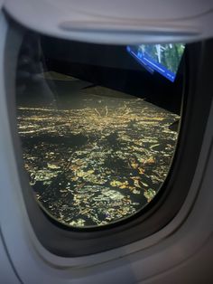 an airplane window looking out at the city lights in the sky and land below it