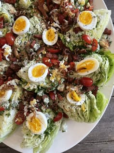 a white plate topped with lettuce covered in hard boiled eggs, bacon and tomatoes