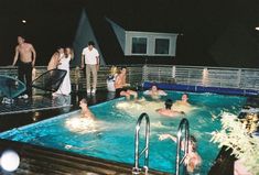 several people are in the pool at night, one person is standing up and two others are sitting down