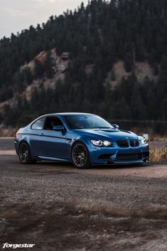 the blue car is parked on the side of the road in front of a mountain