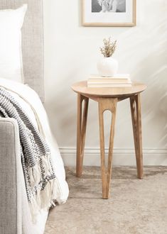 a small wooden table sitting in front of a bed next to a white wall with a black and white photo on it