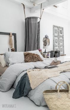 a bed with blankets, pillows and bags on it in a room that has white walls