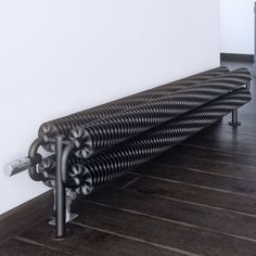 a long metal radiator sitting on top of a wooden floor next to a white wall