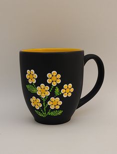 a black mug with yellow and white flowers painted on the inside is sitting in front of a gray background