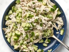 a blue bowl filled with cucumber and chicken salad on top of a white table