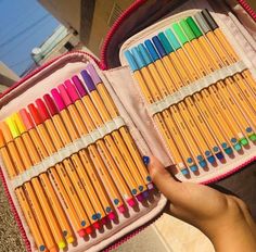 a pink case filled with lots of colorful crayon pencils next to a person's hand