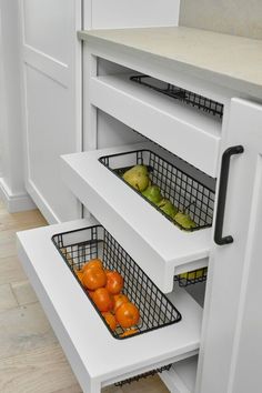 an open drawer in a white kitchen with fruit and vegetables inside the bins on the bottom shelf