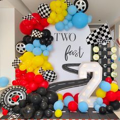 a birthday decoration with balloons and race cars on the table in front of a sign that says two fast