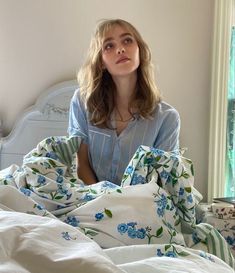 a woman is sitting in bed with white sheets and blue flowers on the comforter