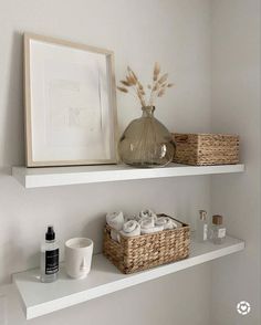 two white shelves with baskets and towels on them in a bathroom area next to a framed photograph