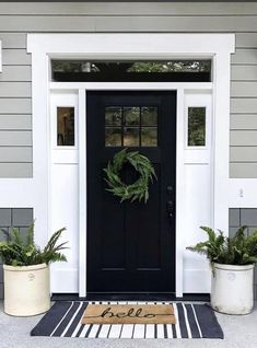 a black front door with a welcome mat and two white planters on the side